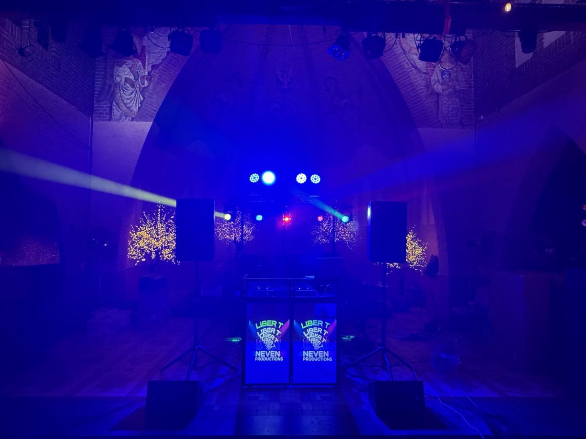 DJ-booth met twee speakers en moving heads op truss